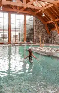 Mujer disfrutando de la piscina termal techada en el Hotel Termas de Puyehue, con arquitectura de madera y piedra